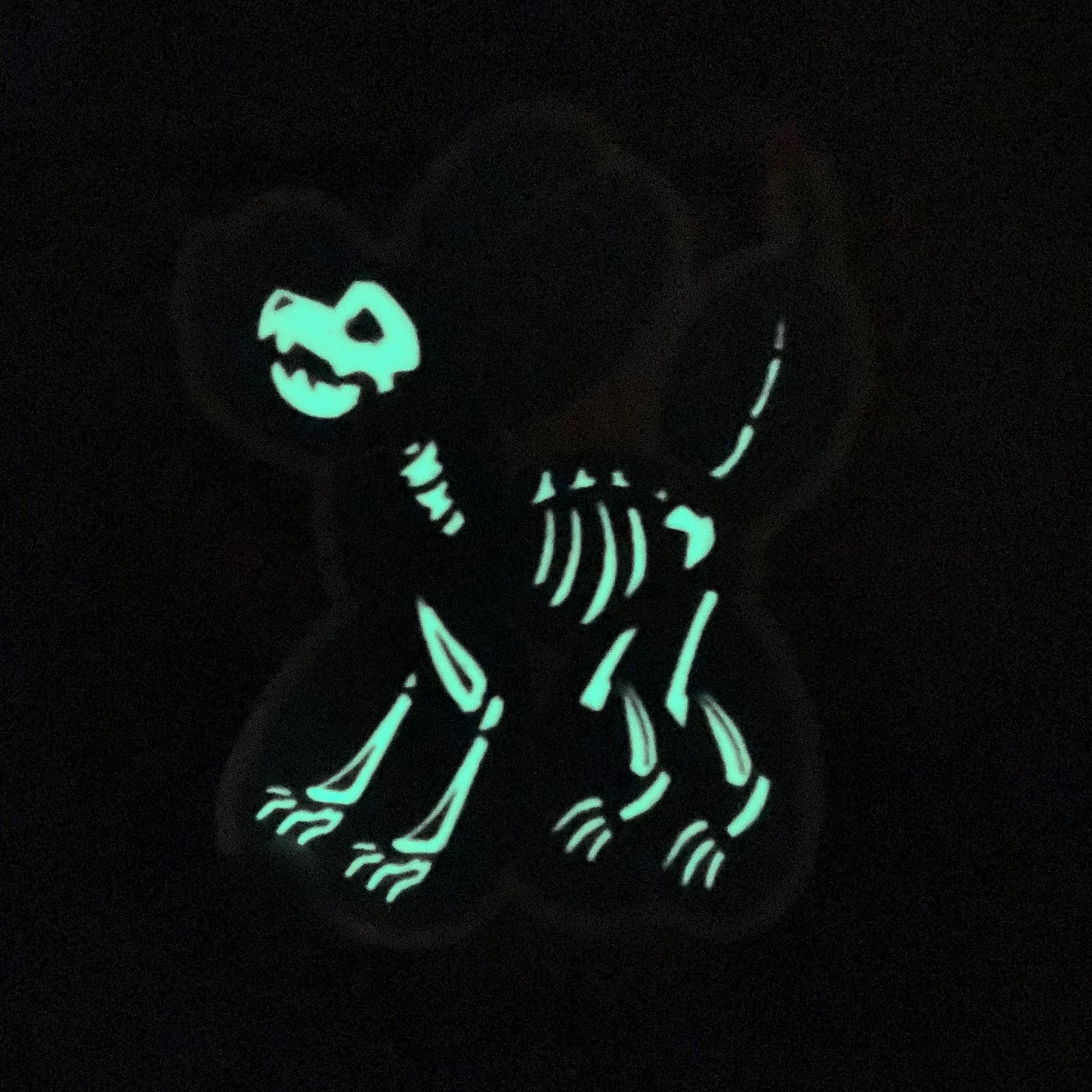 A vinyl sticker featuring a black balloon animal dog with a glow-in-the-dark white skeleton inside it. The lights are turned off so that the glow is featured.