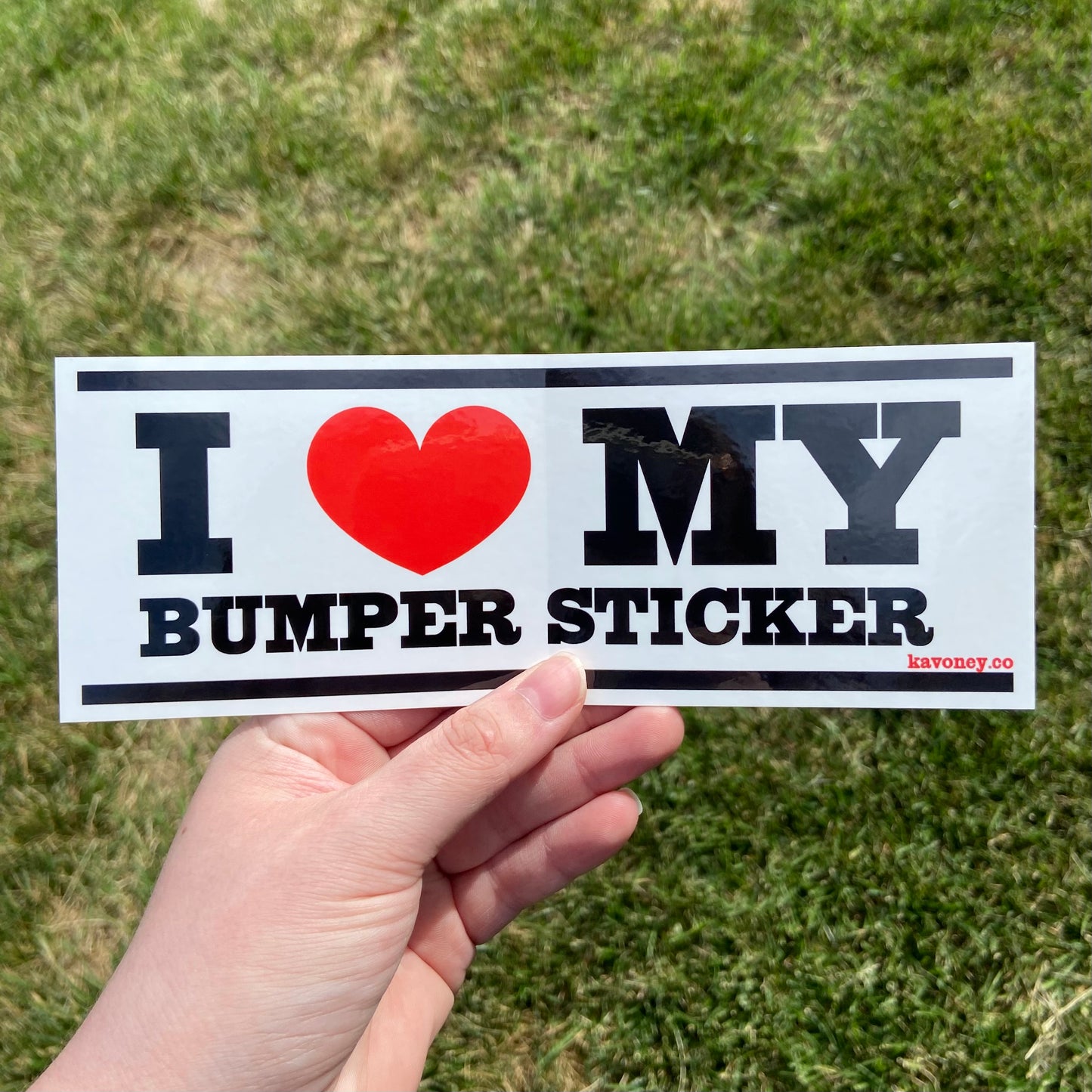 A white rectangular vinyl sticker featuring large black text that reads “I LOVE MY BUMPER STICKER” with a bright red heart in place of the word “love”. There are black bars at the top and bottom of the sticker.
