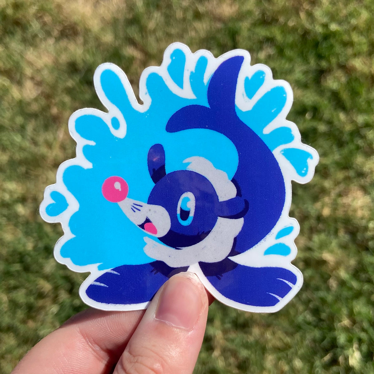 A vinyl sticker featuring an illustration of a cute blue sea lion monster! It has a white collar and is surrounded by decorative blue water.