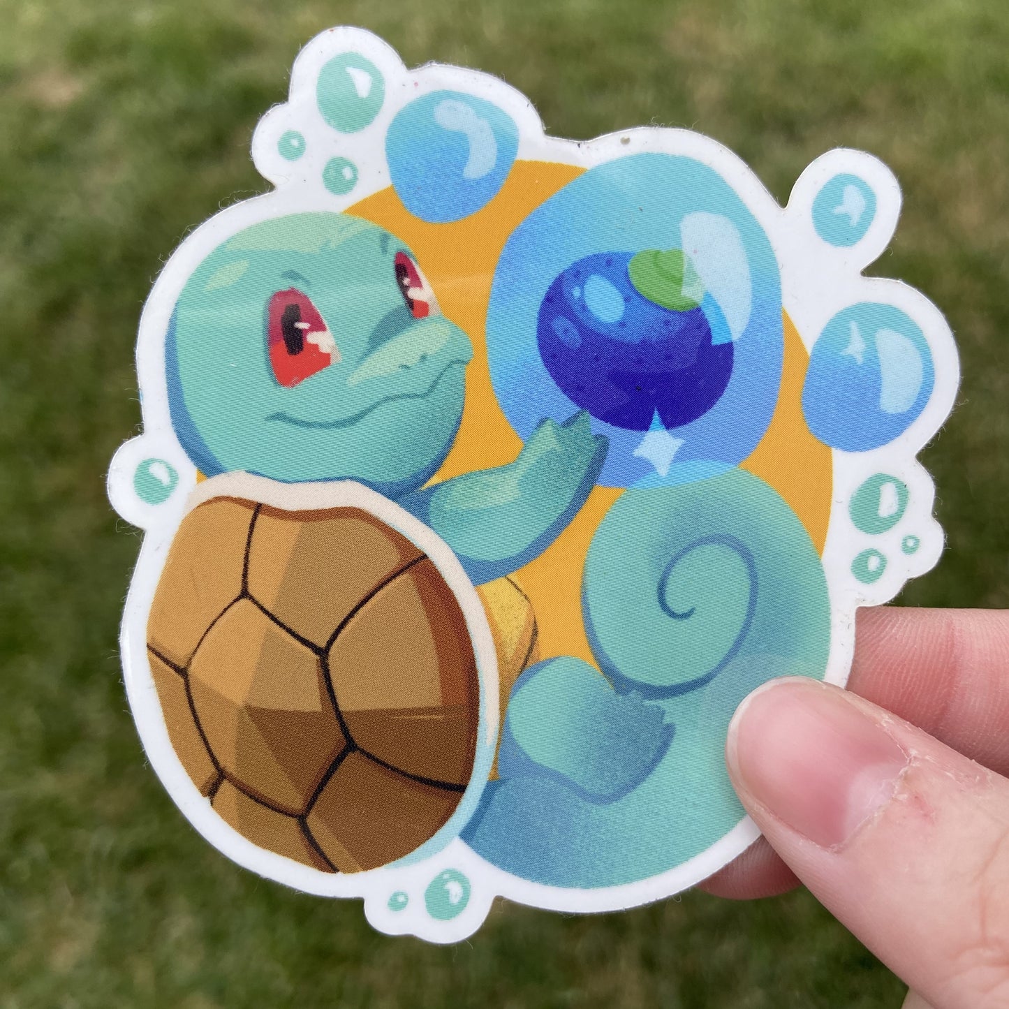 A vinyl sticker of the Pokemon Squirtle and an Oran berry, an in-game item. Squirtle is holding the berry in a floating water bubble alongside it.