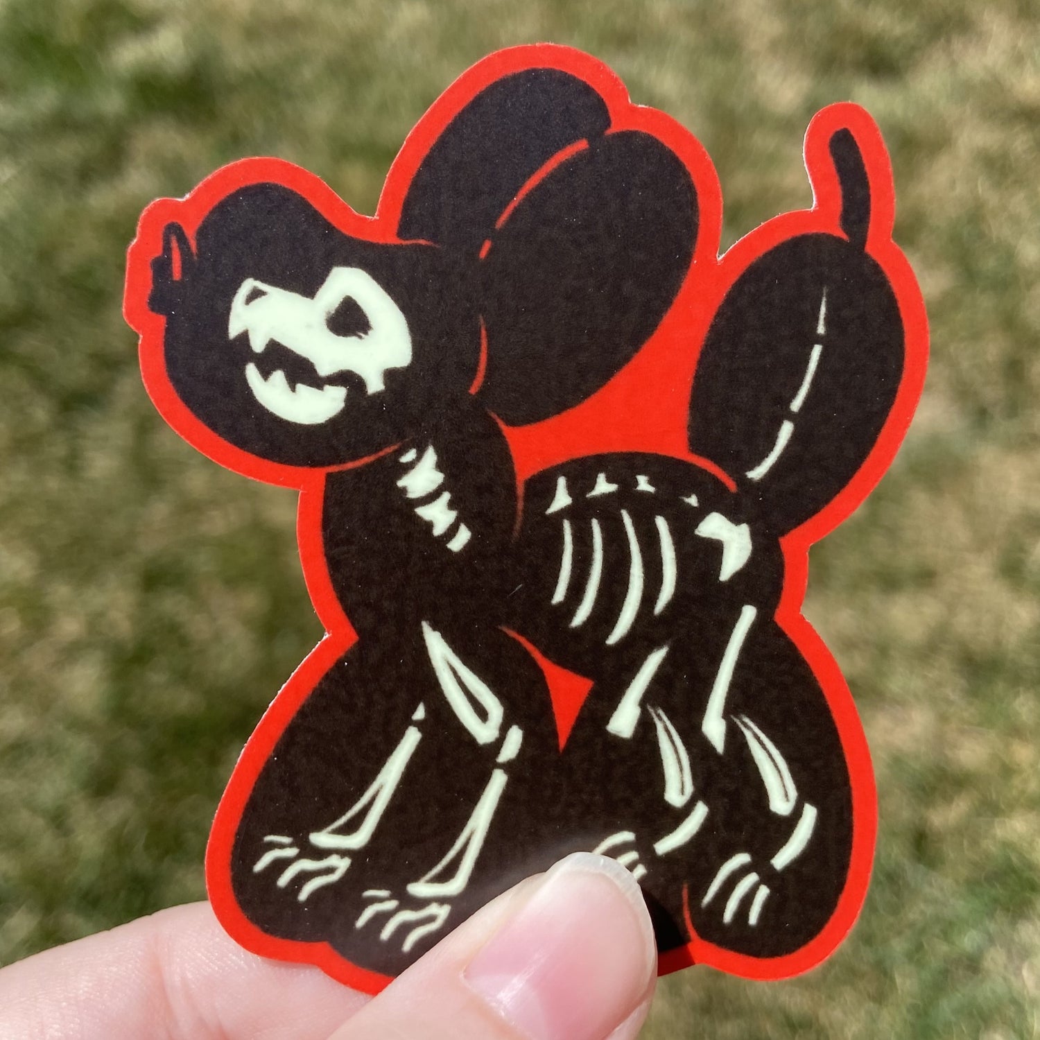 A vinyl sticker featuring a black balloon animal dog with a white skeleton inside it. The border around the balloon animal is bright red.