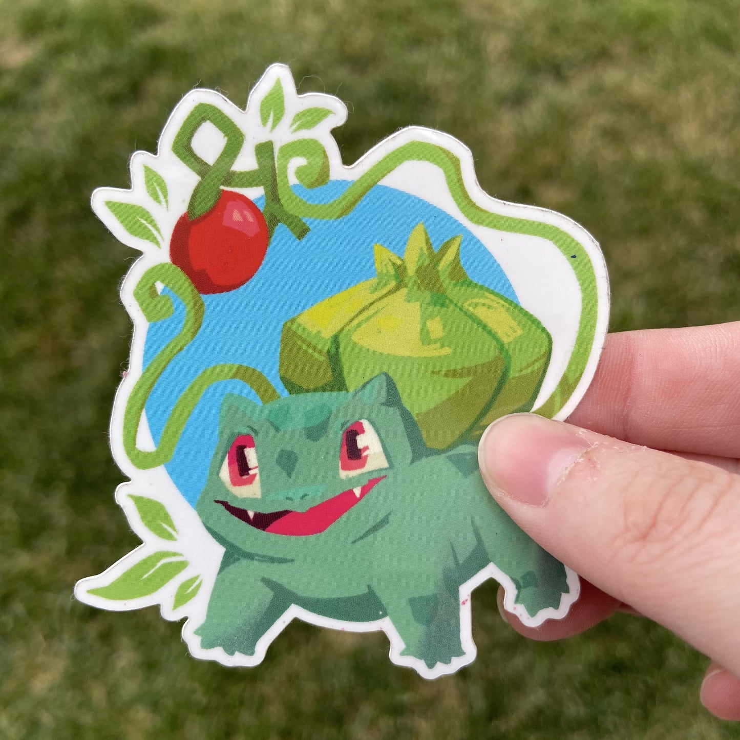 A vinyl sticker of the Pokemon Bulbasaur and a Cheri berry, an in-game item. Bulbasaur is holding the berry with its vines.