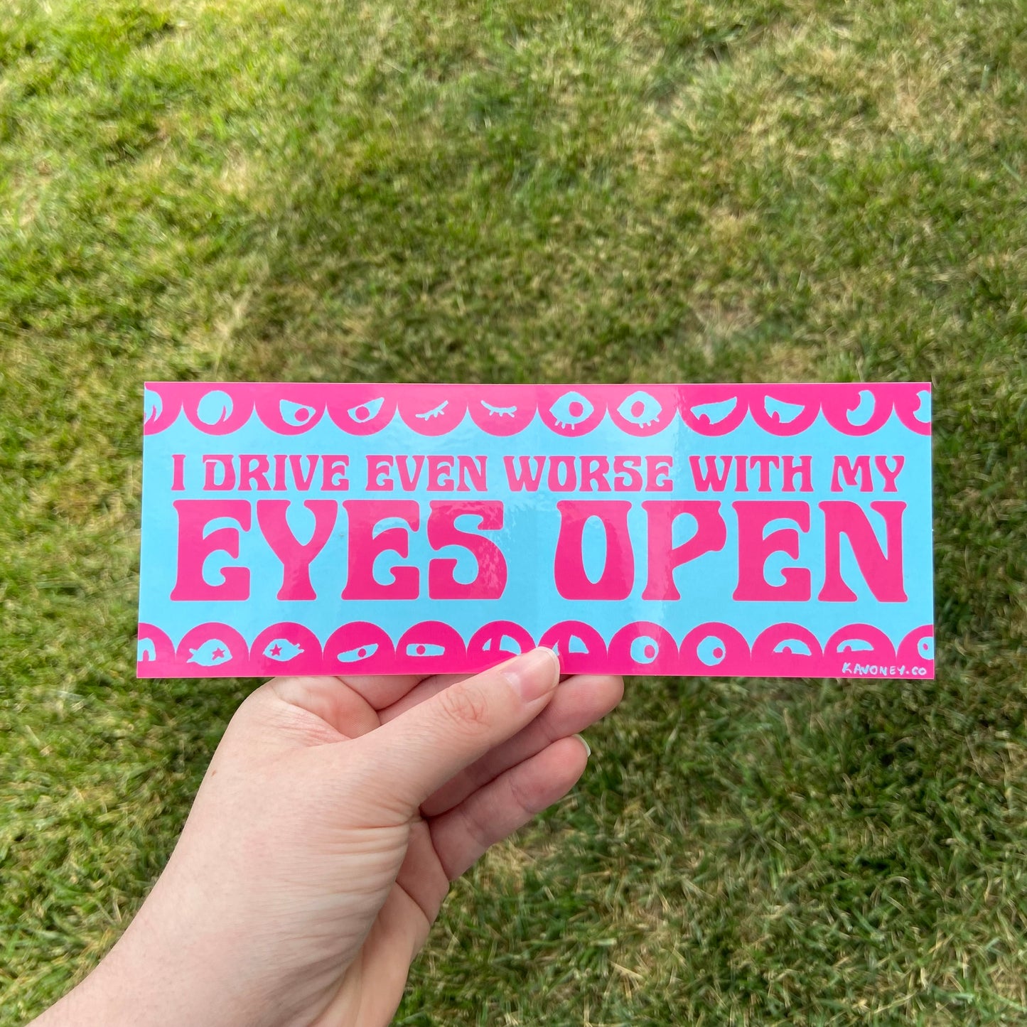 A baby blue rectangular vinyl sticker featuring large text in a decorative font that reads “I drive even worse with my eyes open” in magenta. At the top and bottom are scalloped borders with illustrated pairs of eyes looking in all sorts of directions.