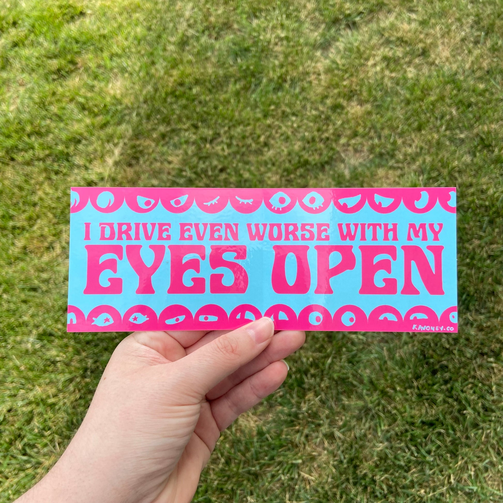 A baby blue rectangular vinyl sticker featuring large text in a decorative font that reads “I drive even worse with my eyes open” in magenta. At the top and bottom are scalloped borders with illustrated pairs of eyes looking in all sorts of directions.