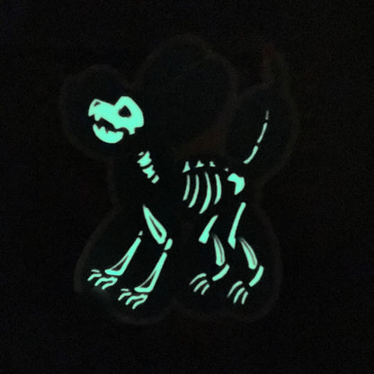 A vinyl sticker featuring a black balloon animal dog with a glow-in-the-dark white skeleton inside it. The lights are turned off so that the glow is featured.