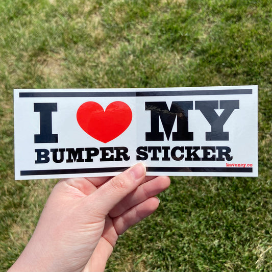 A white rectangular vinyl sticker featuring large black text that reads “I LOVE MY BUMPER STICKER” with a bright red heart in place of the word “love”. There are black bars at the top and bottom of the sticker.