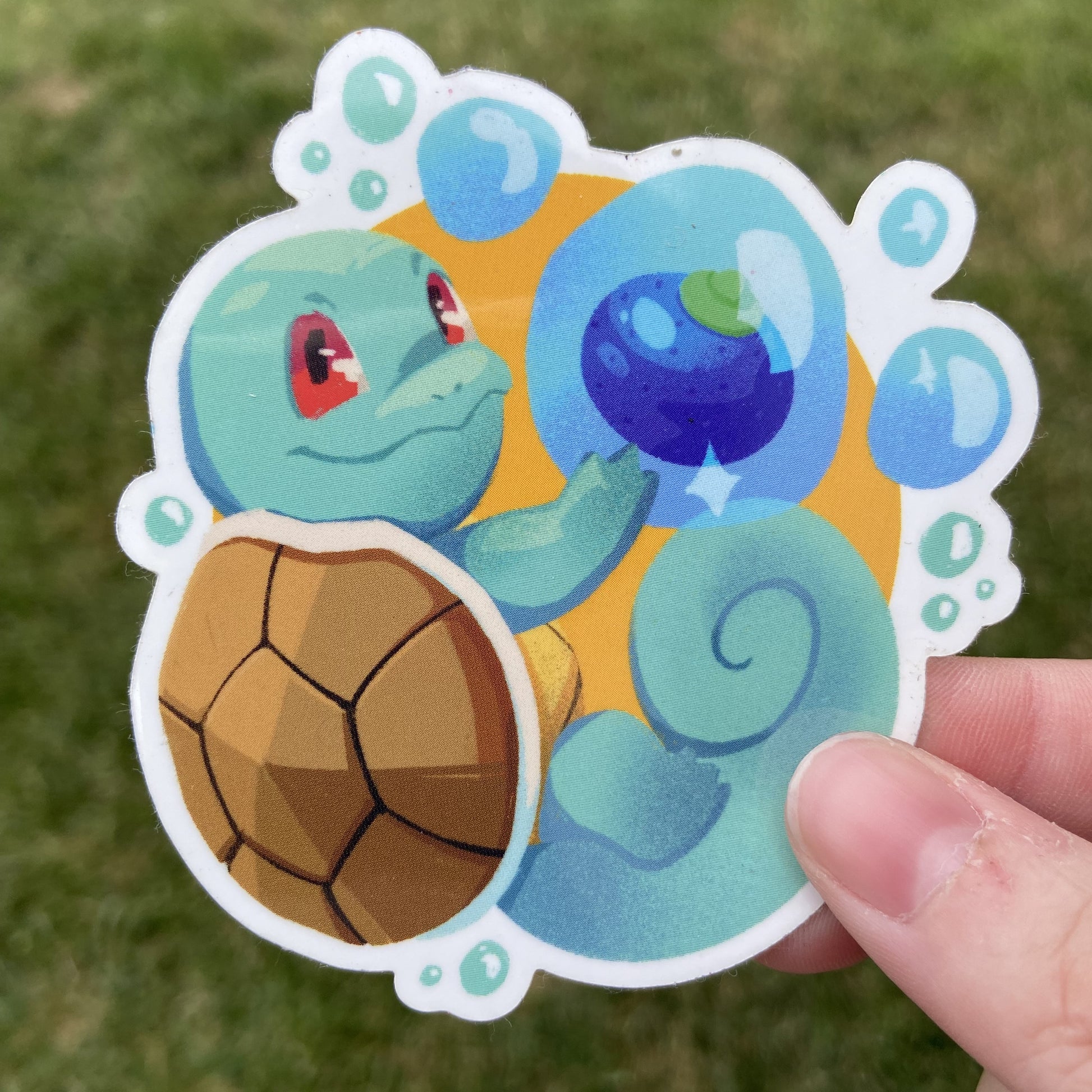 A vinyl sticker of the Pokemon Squirtle and an Oran berry, an in-game item. Squirtle is holding the berry in a floating water bubble alongside it.
