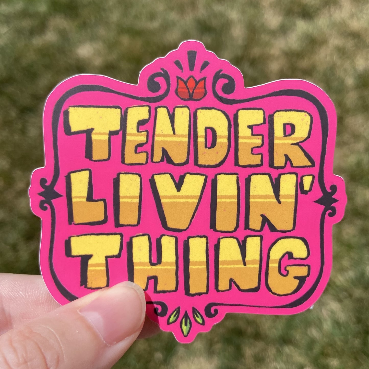 A vinyl sticker featuring large yellow text that reads “TENDER LIVIN’ THING”. There is an embellished brown border around the text and small flower details at the top and bottom.