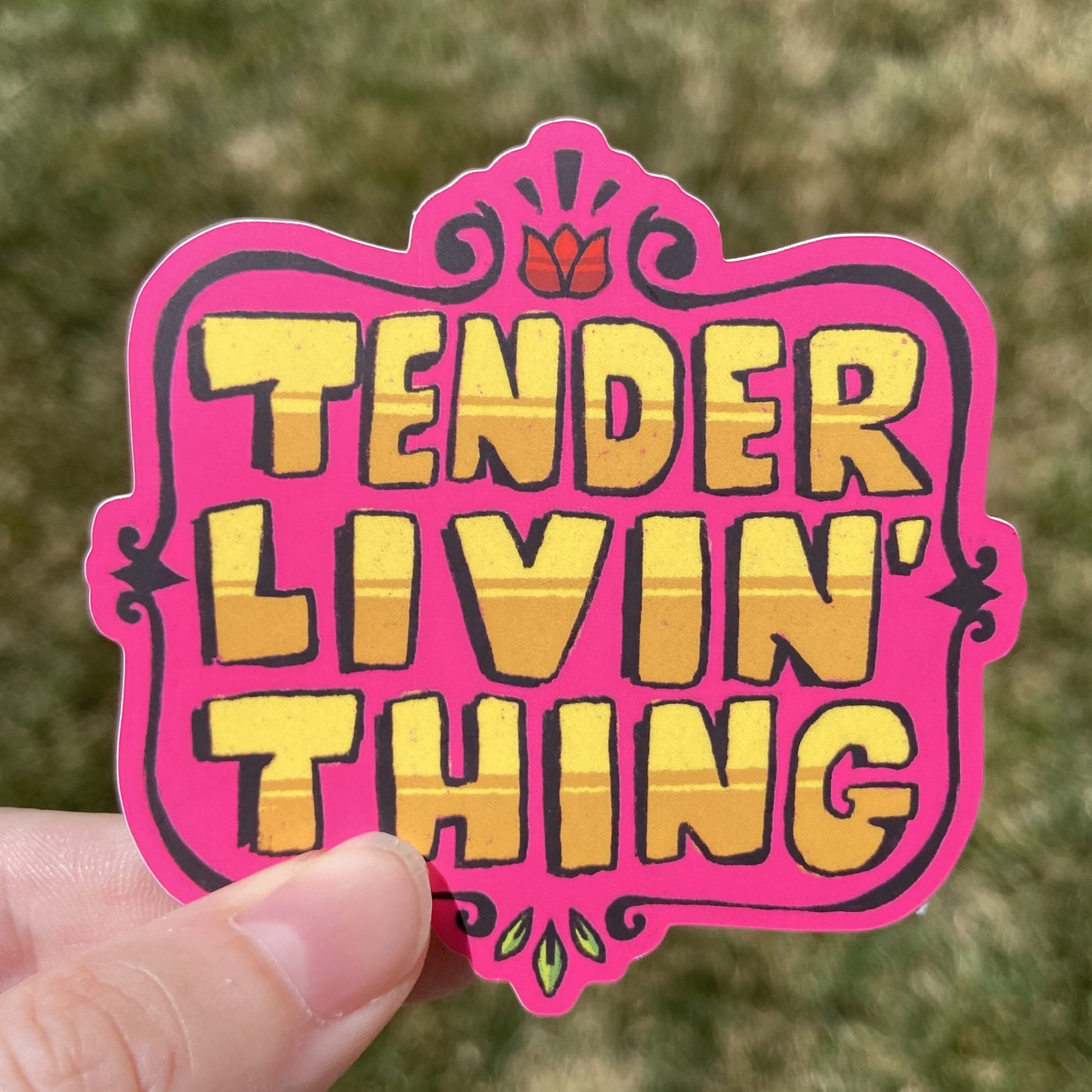 A vinyl sticker featuring large yellow text that reads “TENDER LIVIN’ THING”. There is an embellished brown border around the text and small flower details at the top and bottom.