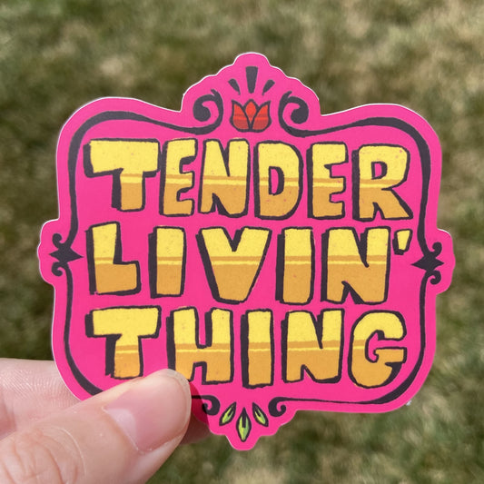 A vinyl sticker featuring large yellow text that reads “TENDER LIVIN’ THING”. There is an embellished brown border around the text and small flower details at the top and bottom.